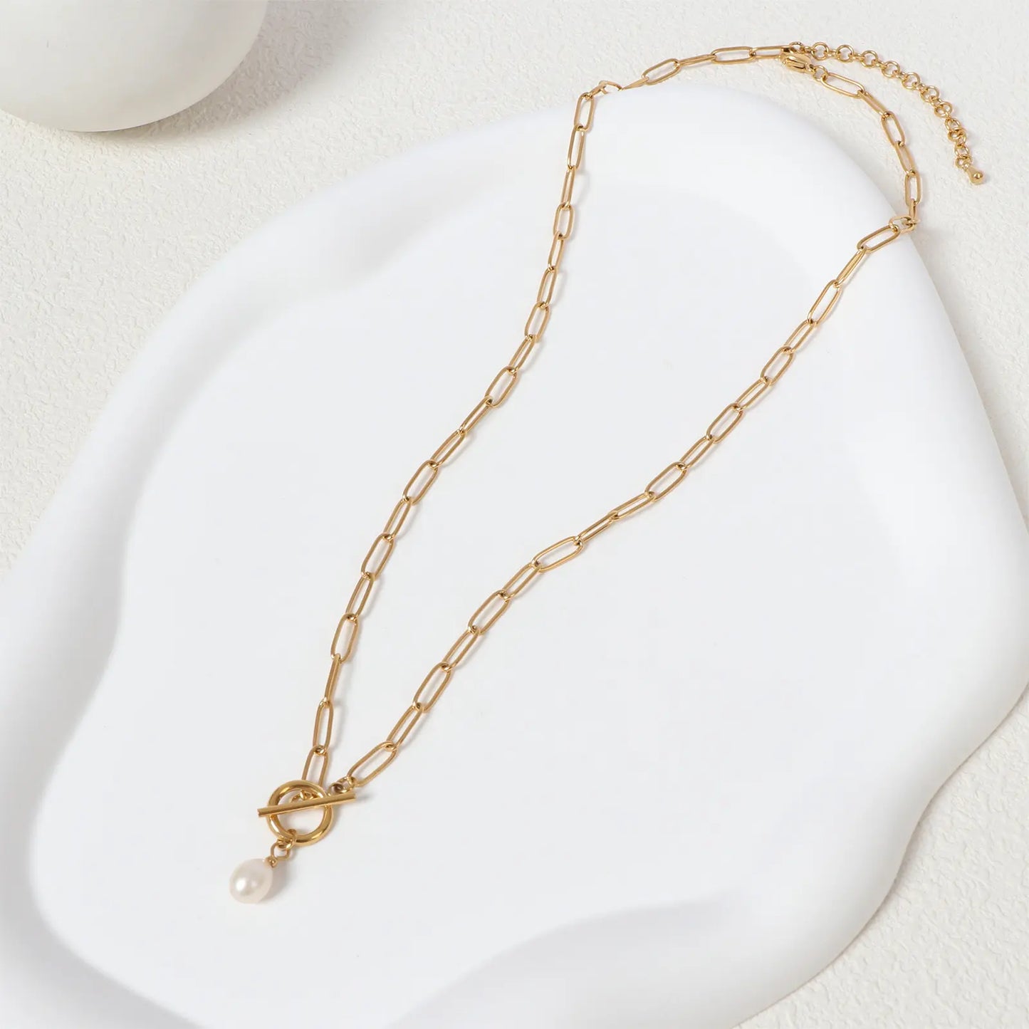 Elegant flat lay display of the MEHRZEB 18k gold paperclip chain and natural baroque pearl resting on a white aesthetic prop.
