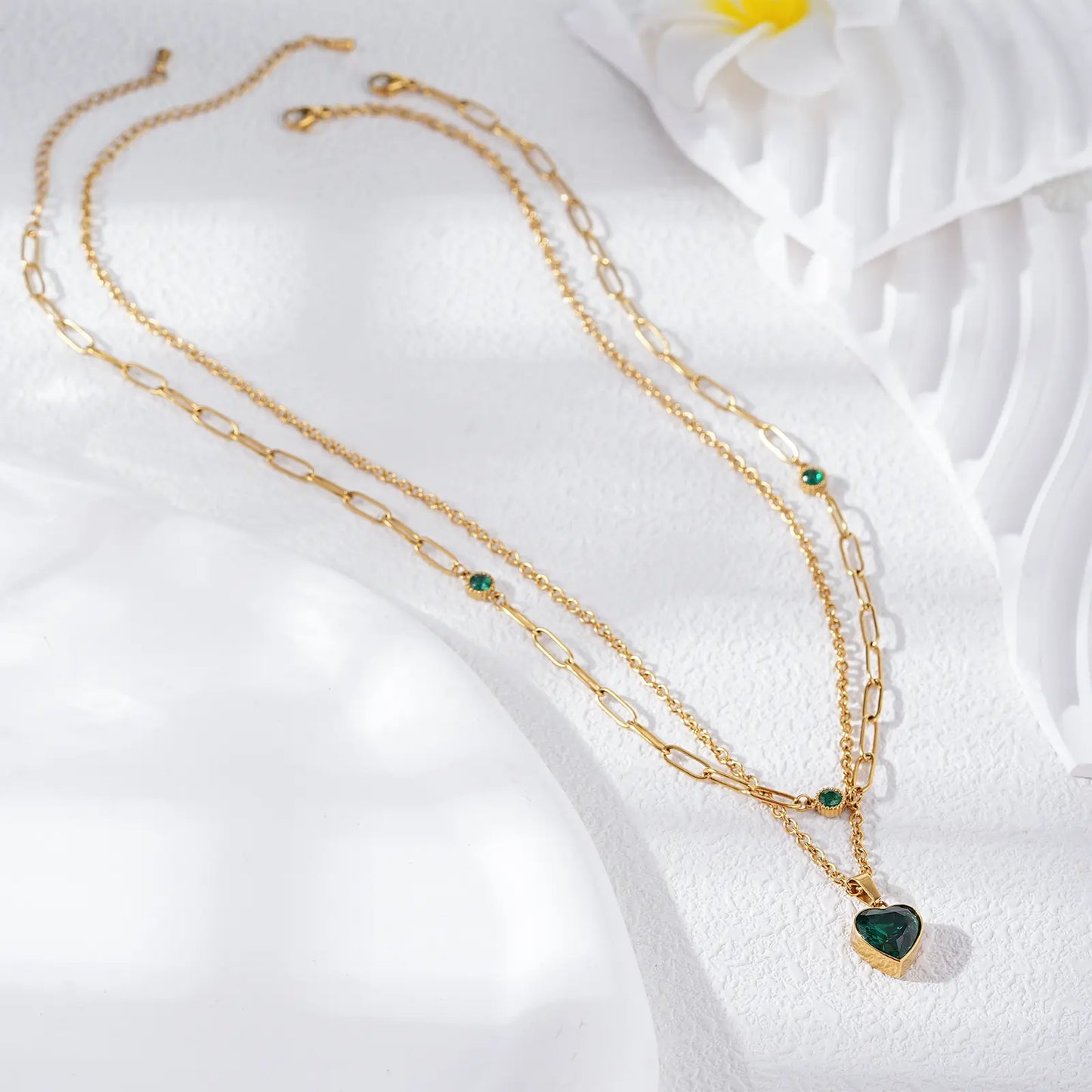 Flat lay aesthetic view of the MEHRZEB waterproof 18k gold double layered necklace with green stones.