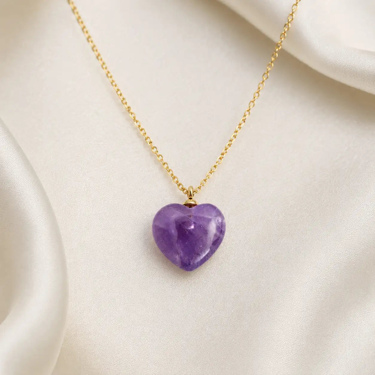 Flat lay aesthetic view of the MEHRZEB amethyst heart necklace resting on premium white silk fabric.