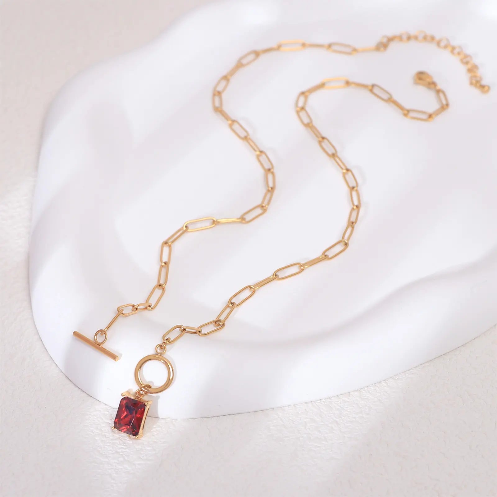 Flat lay aesthetic view of the MEHRZEB waterproof 18k gold paperclip chain and red pendant.