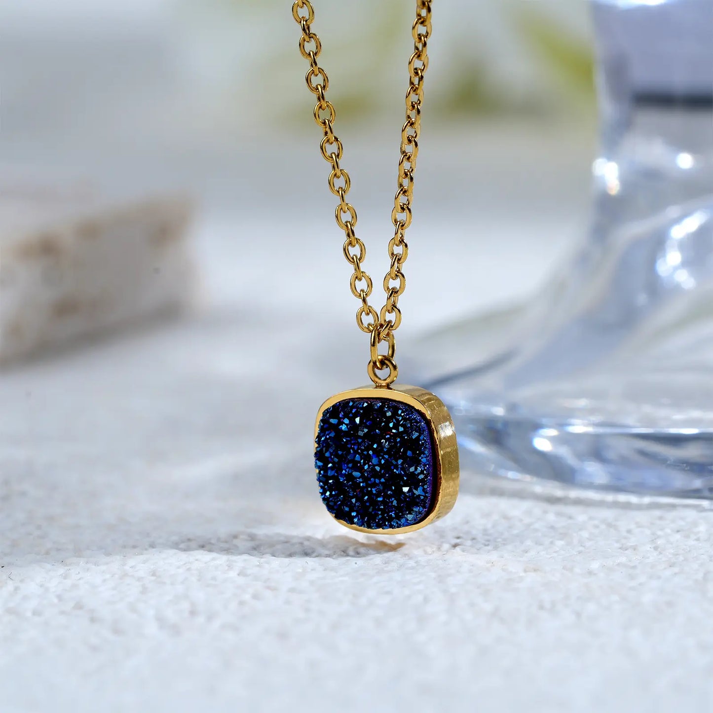 Close up shot of the sparkling sapphire blue druzy stone and 18k gold plating on the MEHRZEB cushion pendant.