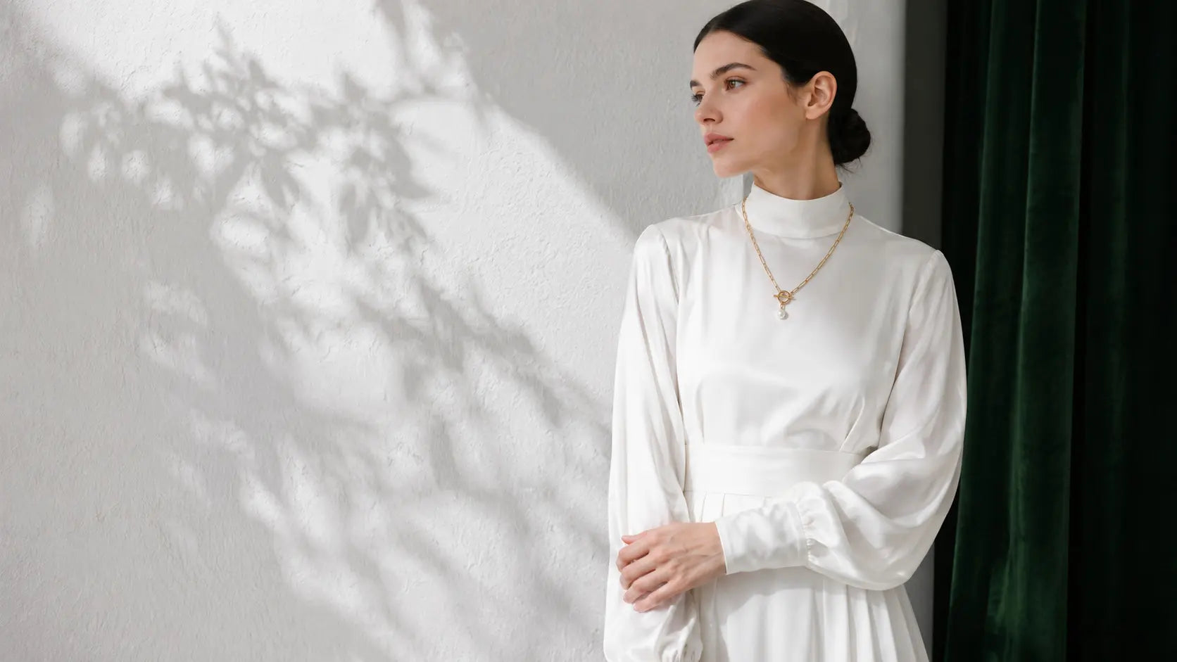 Elegant woman wearing MEHRZEB premium gold paperclip chain necklace with a pearl toggle pendant, dressed in white silk.